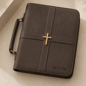 May include: A dark brown rectangular Bible cover featuring a smooth matte finish, a sturdy side handle, and a gold-toned metal cross centered on the front. The name ALEX JR. is embossed in the bottom right corner with clean, dark lettering.