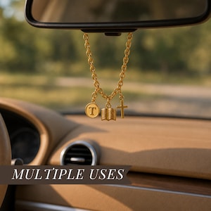 May include: A gold-toned metal car charm hanging from a rearview mirror, featuring a chain with three dangling pendants: a circular charm with the letter T, an open book charm, and a cross charm. The text MULTIPLE USES is visible at the bottom.