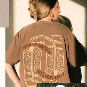 May include: Brown t-shirts with religious-themed graphics. One shirt features a boot design with the text "Hold Up Partner, Let's Pray First." Another shirt has a wave graphic and text. The image also includes the text "Bold Faith Apparel for Every Day Evangelism."