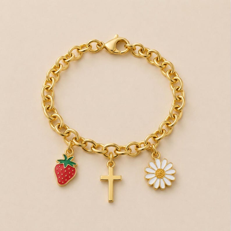 May include: A gold-toned chain link bracelet featuring three dangling charms: a red and green enameled strawberry, a plain gold-toned cross, and a white and yellow enameled daisy flower. The bracelet is secured with a lobster claw clasp.