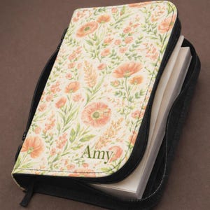 May include: A white ceramic mug with a black handle and the text "But First, Coffee" in a bold, black font. The mug is set against a blurred background, suggesting a cosy setting.