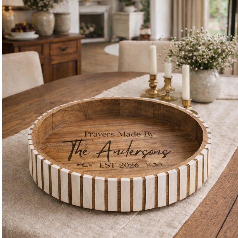 May include: A round wooden tray with a light brown interior and a white and brown striped exterior. The tray has the text "Prayers Made By The Andersons EST 2026" in black script. The tray is on a table with other decorative items.