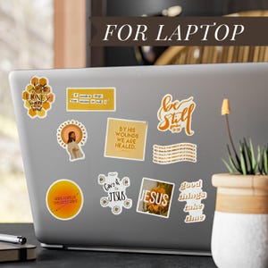 May include: A laptop covered in various stickers with religious themes. The stickers feature phrases like "Be Still", "Jesus", and "By His Wounds We Are Healed". Other stickers have floral and honeycomb designs.