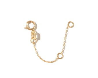May include: A gold-colored necklace extender with a lobster clasp and a delicate chain. The extender features two small rings and a chain, designed to add length to necklaces or bracelets.