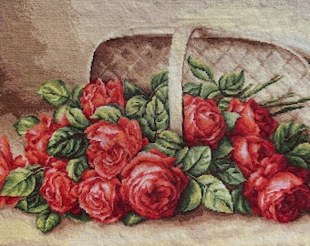 Op de afbeelding: Een tapijt met een mand vol rode rozen en groene bladeren. De mand is beige met een gewatteerd patroon en een witte handgreep. De rozen staan in volle bloei en vormen een levendig bloemstuk.