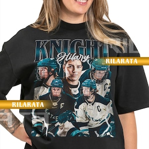 May include: Black adult unisex t-shirt featuring a graphic of a hockey player with the text "KNIGHTS Hilary" and the word "RILARATA". The design includes images of hockey players in teal and white uniforms.
