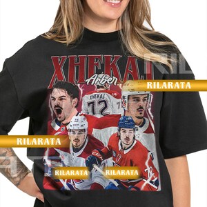 Könnte beinhalten: Schwarzes Unisex-T-Shirt für Erwachsene mit einem Grafikdesign im Vintage-Stil von Eishockeyspielern. Das Design enthält den Text "XHEKAJ" und "Arber" sowie die Nummer 72. Das Shirt hat einen Rundhalsausschnitt und kurze Ärmel.