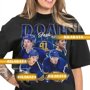 Könnte beinhalten: Schwarzes Unisex-T-Shirt für Erwachsene mit einer Grafik eines Eishockeyspielers in blau-weißer Uniform. Das Shirt hat den Namen "DOAN" und die Nummer "91" aufgedruckt. Der Text "RILARATA" ist ebenfalls sichtbar.