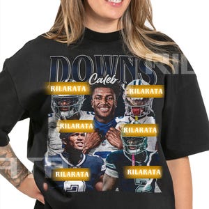 Op de afbeelding: Zwart unisex T-shirt met een grafisch ontwerp met de tekst "DOWNS" en "Caleb". Het ontwerp bevat afbeeldingen van American football spelers en het woord "RILARATA". Het shirt wordt omschreven als een unisex T-shirt voor volwassenen.