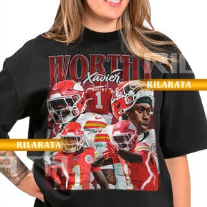 Puede incluir: Camiseta unisex para adultos de color negro con un gráfico de jugadores de fútbol americano con uniformes y cascos rojos y blancos. La palabra "WORTHY" está impresa en rojo, con el nombre "Xavier" encima del número "1". La camiseta incluye el texto "RILARATA".