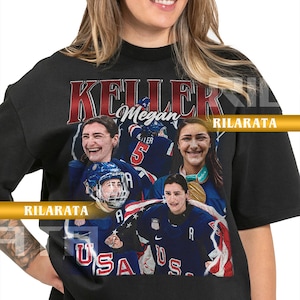 May include: Black unisex t-shirt featuring a collage of images and the name "KELLER" in red. The shirt includes the text "Megan" and "USA" in white. The design incorporates images of a person in a sports uniform.