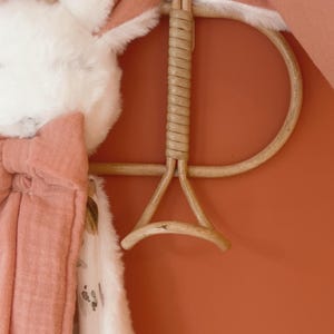 May include: A soft, plush security blanket featuring a white faux fur texture and a dusty rose-colored fabric with a floral pattern. The blanket is draped over a light brown, curved rattan wall hook, showcasing its layered, multi-textured design.