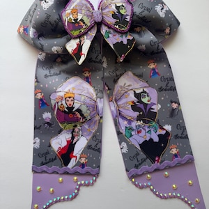 May include: A large hair bow made of grey grosgrain ribbon featuring a repeating pattern of Disney villains and the text Cruel & Beautiful. The bow includes a central glittery purple accent, scalloped lavender trim, and small clear rhinestones.