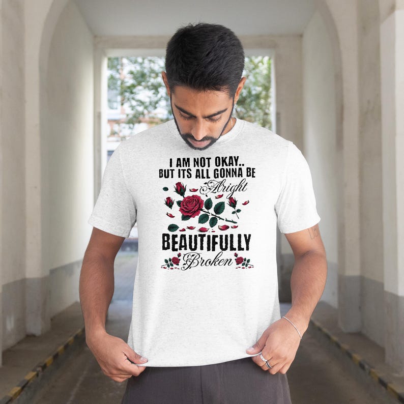 May include: A light gray t-shirt with the text "I AM NOT OKAY.. BUT ITS ALL GONNA BE Alright BEAUTIFULLY Broken" in black and red. The design includes a red rose and rosebuds.
