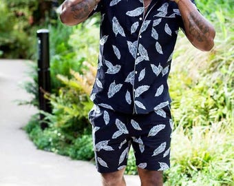 Puede incluir: Un conjunto de camisa de manga corta con botones y pantalón corto a juego, de color negro con un estampado de plumas blancas. La camisa incluye un cuello con muesca, un bolsillo delantero y botones blancos. El pantalón tiene cintura elástica.
