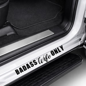 May include: White car door sill with the text "BADASS Wife ONLY" in black script and block letters. The car door sill is located near the step and the interior of the car.