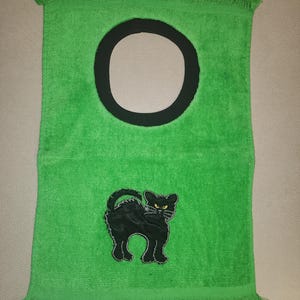 May include: Green towel with a black cat and a black circle in the center. The towel has a fringe border.