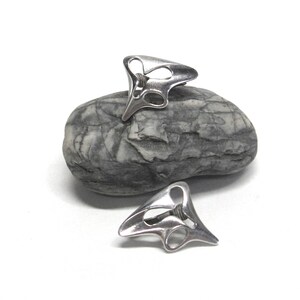 May include: A pair of silver abstract earrings with a unique, organic design. The earrings are made of metal and have a smooth, polished finish.
