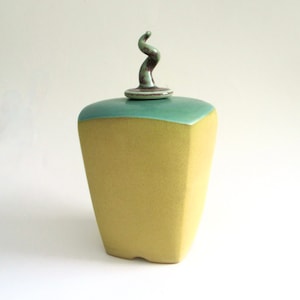 May include: A yellow ceramic jar with a green lid and a swirling green ceramic knob on top.