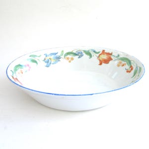 May include: White ceramic bowl with a blue rim and a floral design featuring blue, orange, yellow, and green flowers.