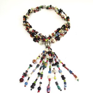 May include: Multi-strand necklace with a tassel made of colorful beads, including black, white, red, green, blue, and brown beads. The necklace has a silver clasp.