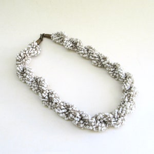 May include: A white beaded necklace with a twisted design. The necklace is made of small, white beads that are strung together in a spiral pattern. The necklace is approximately 18 inches long and has a simple clasp.