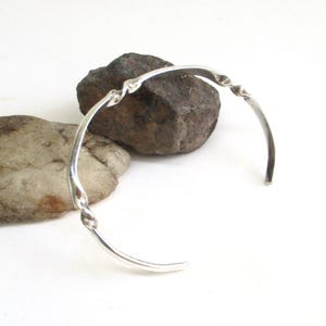 May include: A silver-colored metal cuff bracelet featuring a smooth, polished finish with two distinct twisted sections integrated into the band. The bracelet has an open design, allowing it to be slipped onto the wrist with ease.