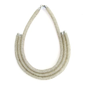 May include: A silver beaded necklace with three strands. The necklace is made of small, round beads that are strung together to create a smooth, flowing look.
