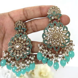 May include: A pair of gold-coloured earrings with turquoise and white detailing. The earrings have a floral design with turquoise stones and white pearl-like beads. The earrings are a dangle style.