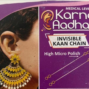 May include: A purple product box for Karna Aadhar Invisible Kaan Chain featuring a high micro polish finish. The packaging displays an illustration of a yellow floral earring and two thin metallic chains with loops at each end for ear support.