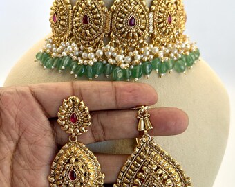 May include: Gold-toned jewelry set featuring a choker necklace, bracelet, and earrings. The necklace and earrings have a teardrop design with red and green accents. The set includes green beads and small white pearls.
