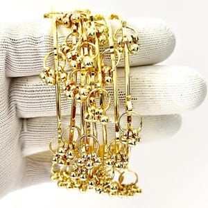 May include: A collection of gold-colored bangles. Each bangle features a series of small, round, gold-colored beads clustered together, and connected by a thin, gold-colored bar. The bangles are displayed against a white background.