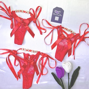 May include: Red lace lingerie with satin ribbon ties and rhinestone accents. The lingerie features the phrases "FUCK ME", "CUSTOM", and "JUICY ASS" across the waistband. A Charming Chic tag is visible.