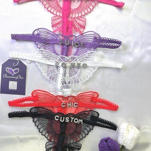 Op de afbeelding: Een verzameling vlindervormige lingerie in roze, paars, wit, rood en zwart. Elk stuk heeft een woord in strass: "YUMMY", "JUICY", "ROMEO", "CHIC" en "CUSTOM". Een "Charming Chic"-label en gehaakte bloemen zijn ook aanwezig.