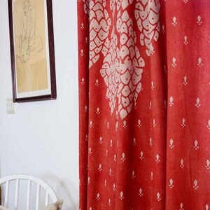 May include: Red fabric curtain with a white pattern of stylized leaves and small white dots. The curtain is hanging in a room with a white wall and a framed drawing.