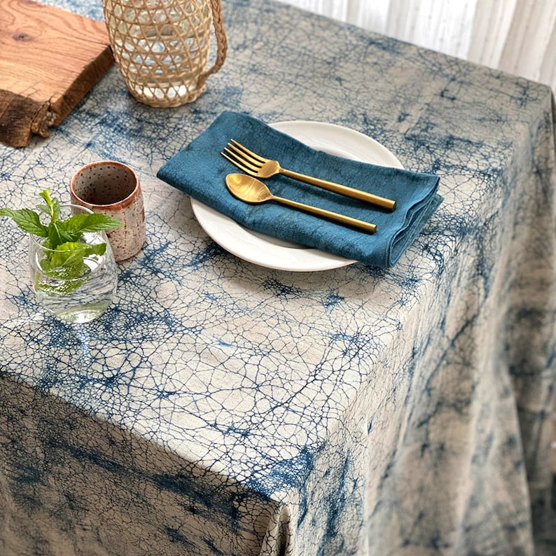 May include: A blue and white tablecloth with a crackled pattern. A white plate with gold silverware and a blue napkin is on the table. A glass of water with fresh mint and a small ceramic cup are also on the table.