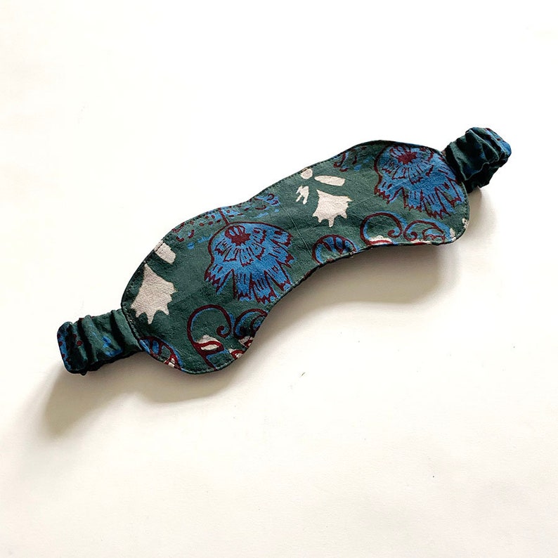 May include: A green sleep mask with a floral pattern in blue and white. The mask has an elastic band for a comfortable fit. The sleep mask is designed to block out light for better sleep.