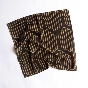 May include: A black cotton tea towel with a gold geometric pattern. The pattern is made up of repeating lines and curves.