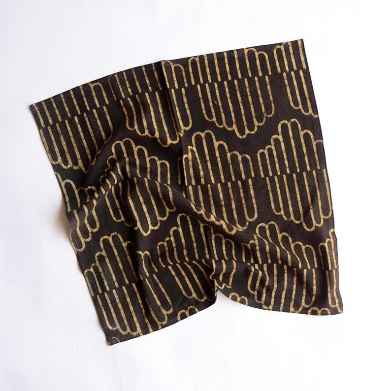 May include: A black cotton tea towel with a gold geometric pattern. The pattern is made up of repeating lines and curves.