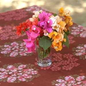 May include: A bouquet of pink, orange and red bougainvillea flowers in a clear glass vase on a brown table with a white floral pattern.