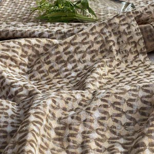 Peut inclure: Gros plan sur un tissu beige avec un motif géométrique brun. Le tissu a une surface légèrement texturée et un léger brillant.