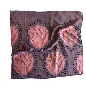 K&ouml;nnte beinhalten: Ein quadratisches, mauvefarbenes Textil mit einem sich wiederholenden Muster aus korallenfarbenen Blumendesigns. Jede Blume ist von einem Kreis aus kleinen, dunkelvioletten Punkten umgeben. Der Stoff ist leicht zerknittert, was auf eine weiche Textur hindeutet.