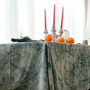 May include: A blue and white patterned tablecloth with a distressed look, featuring three red candles in a ceramic holder and three oranges on the table.