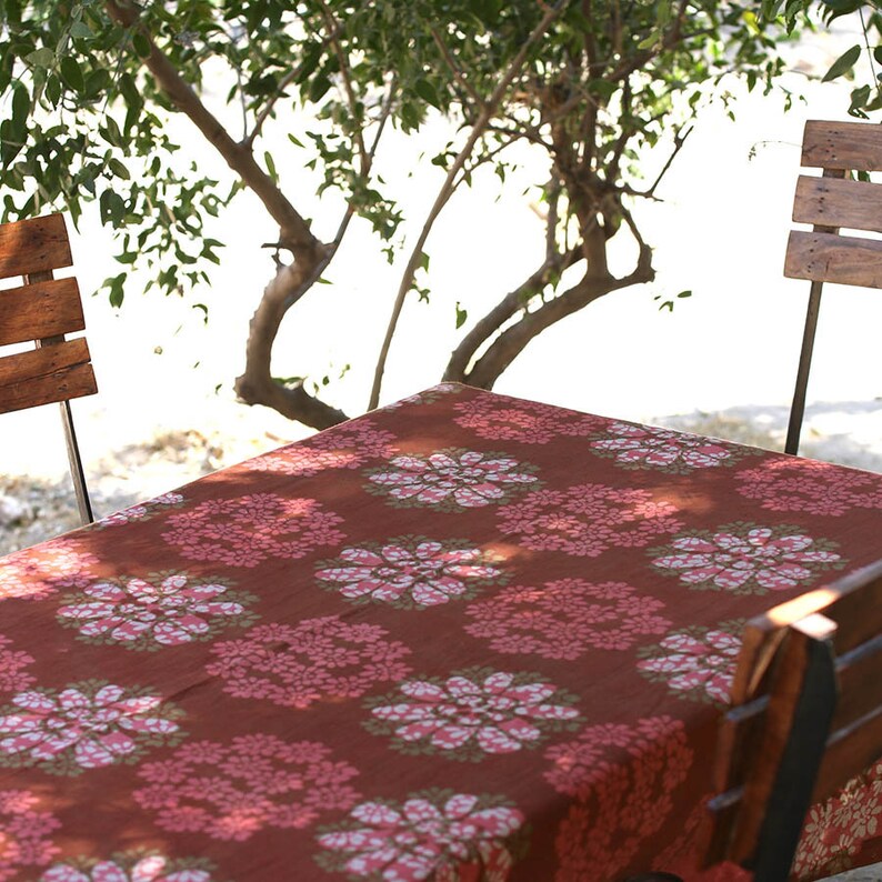 May include: A red and pink floral patterned tablecloth with a white background. The tablecloth is laid out on a table with two wooden chairs.