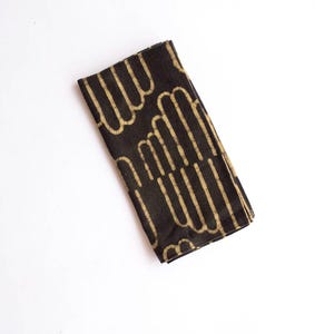 May include: Black cotton napkin with a white geometric pattern. The pattern is made up of repeating lines and curves.