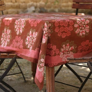 May include: A brown and pink floral tablecloth with a white border. The tablecloth is made of cotton and features a hand-block printed design.
