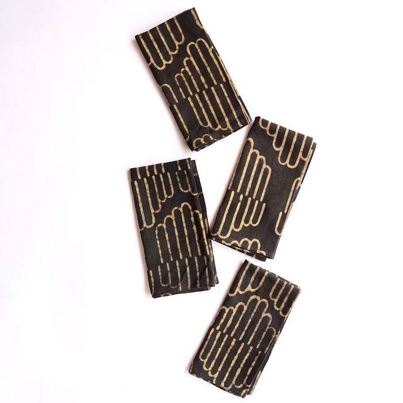 May include: Four black fabric napkins with a gold geometric pattern. The napkins are folded and arranged on a white background.