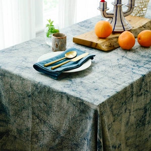May include: A blue and white tablecloth with a crackled pattern. A white plate with a gold knife and spoon is on the tablecloth. There are three oranges on a wooden chopping board.