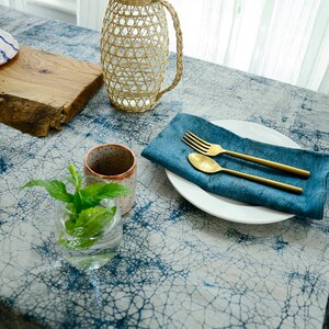 May include: A blue and white patterned tablecloth with a woven pitcher, a ceramic cup, a glass of fresh mint, a white plate, a blue napkin, a fork, and a spoon.
