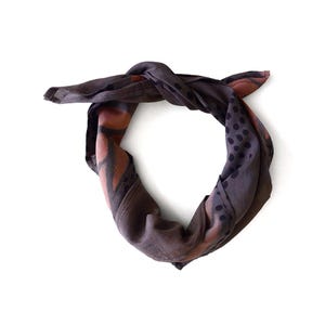 K&ouml;nnte beinhalten: Ein dunkelgraues Bandana mit Knoten. Es zeigt ein Muster aus braunen und schwarzen Formen und Punkten. Der Stoff wirkt weich und leicht, geeignet f&uuml;r verschiedene Styling-Optionen. Ein vielseitiges Accessoire.